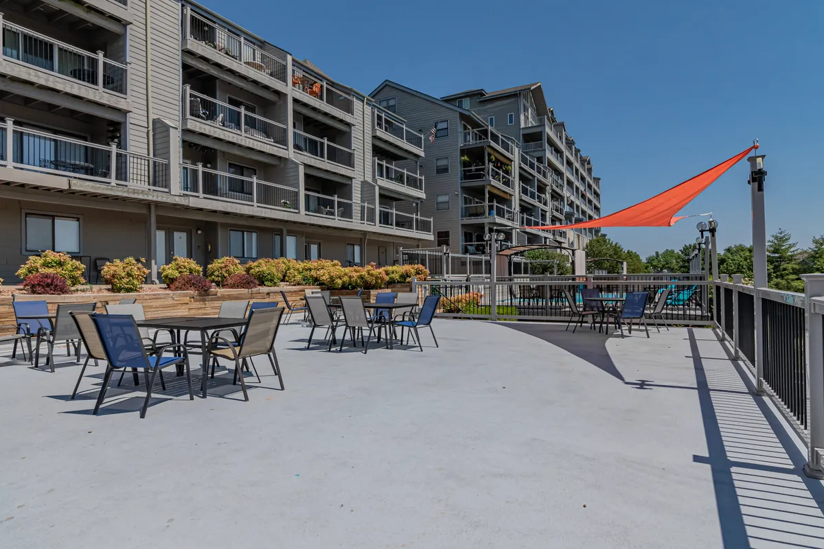 A cheerful exterior scene featuring comfortable outdoor furniture, bright flowers, and a shade sail, designed for socializing and enjoying sunny afternoons. The setup encourages group gatherings, outdoor dining, and fun with friends or family.