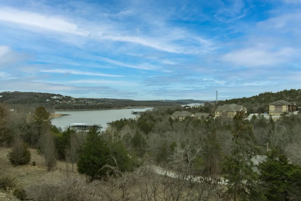 This image presents a wide view of Table Rock Lake, with calm waters, a distant tree line, and gentle hills beyond. Residential properties appear along the shoreline, evoking a serene, natural lakeside setting. The atmosphere is tranquil, ideal for relaxation and peaceful observation.