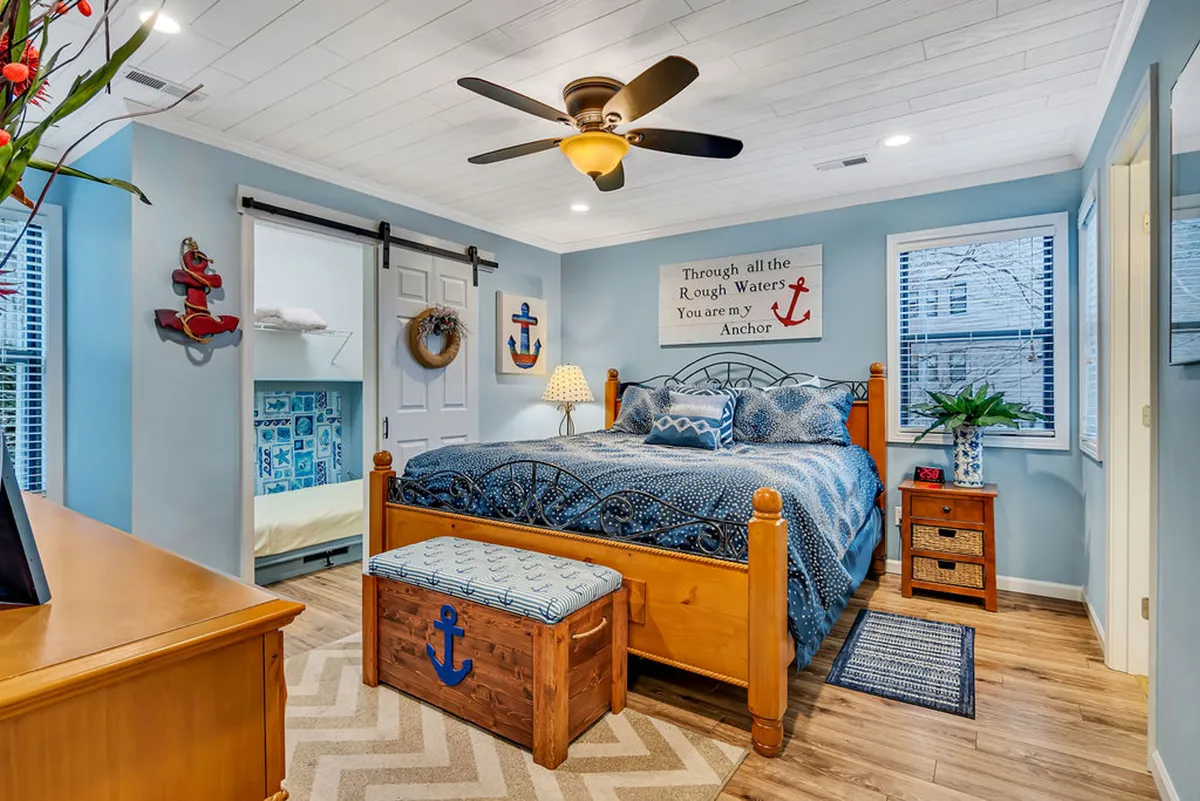 A peaceful bedroom scene with a decorative bed, accent pillows, a wooden anchor-themed bench, and nautical wall decor. The atmosphere is serene, evoking restful nights and gentle mornings.