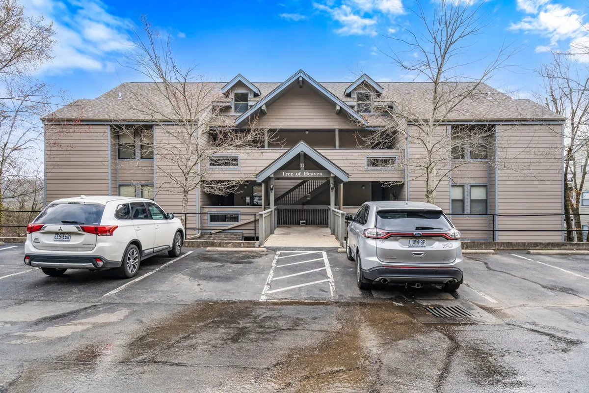 The exterior of the condo building with a clear view of the entrance, parking area, and leafy surroundings. The area is well-kept and welcoming, ideal for easy arrival and convenient access to amenities like boat/trailer parking.