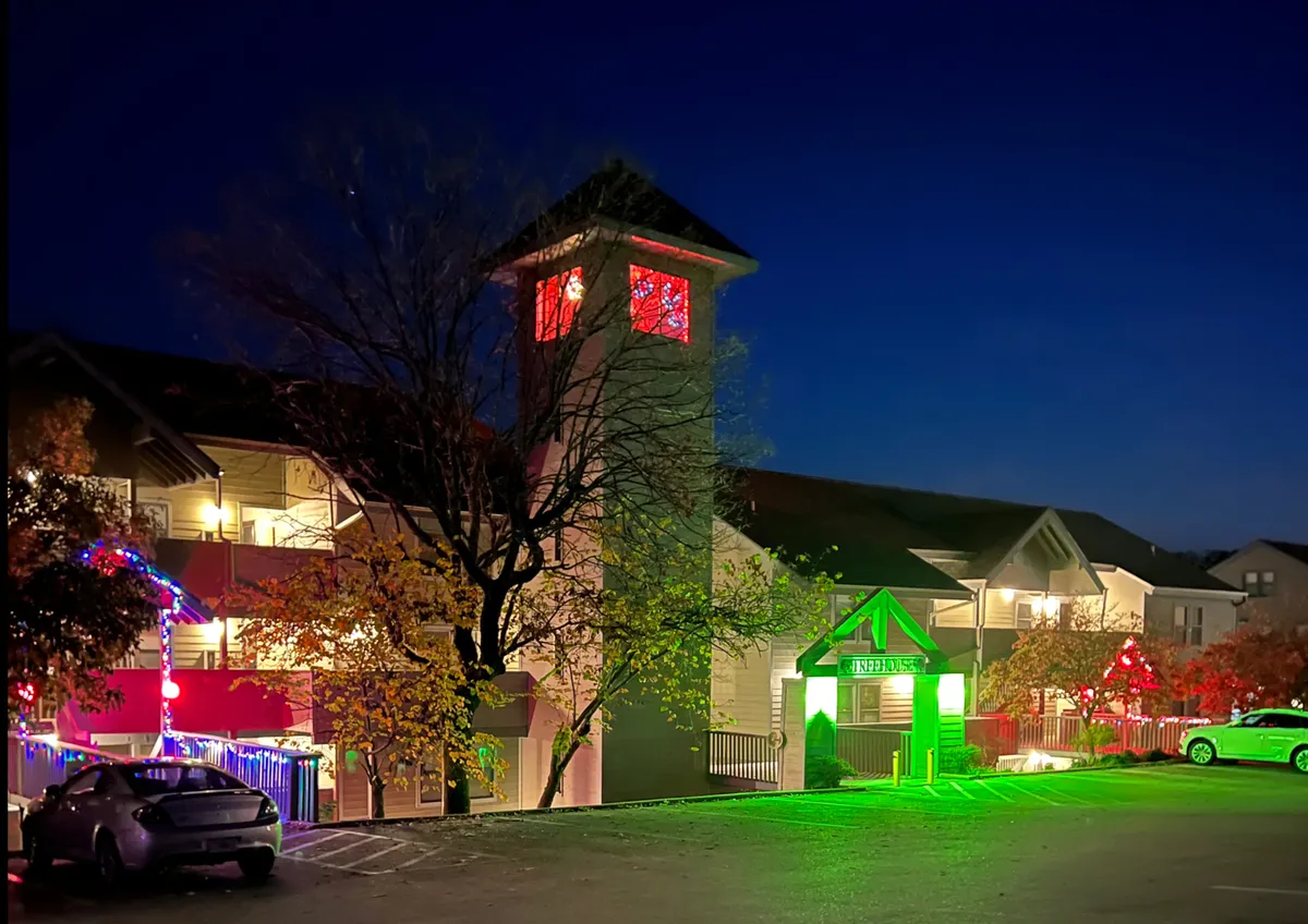 A lively exterior shot capturing decorative lights, a landmark clock tower, and an entrance sign. The scene suggests festive evenings, holiday gatherings, and a welcoming communal atmosphere, with visual cues that evoke nighttime entertainment and community events.