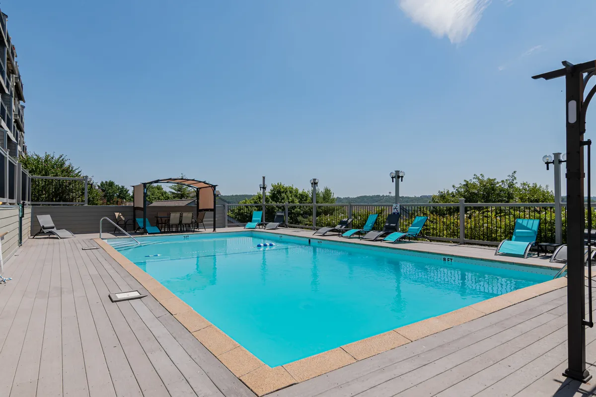 A vibrant outdoor pool area featuring clear blue water, inviting lounge chairs, a charming gazebo, and lush landscape views. The space is designed for family fun and relaxation, evoking resort-style amenities.