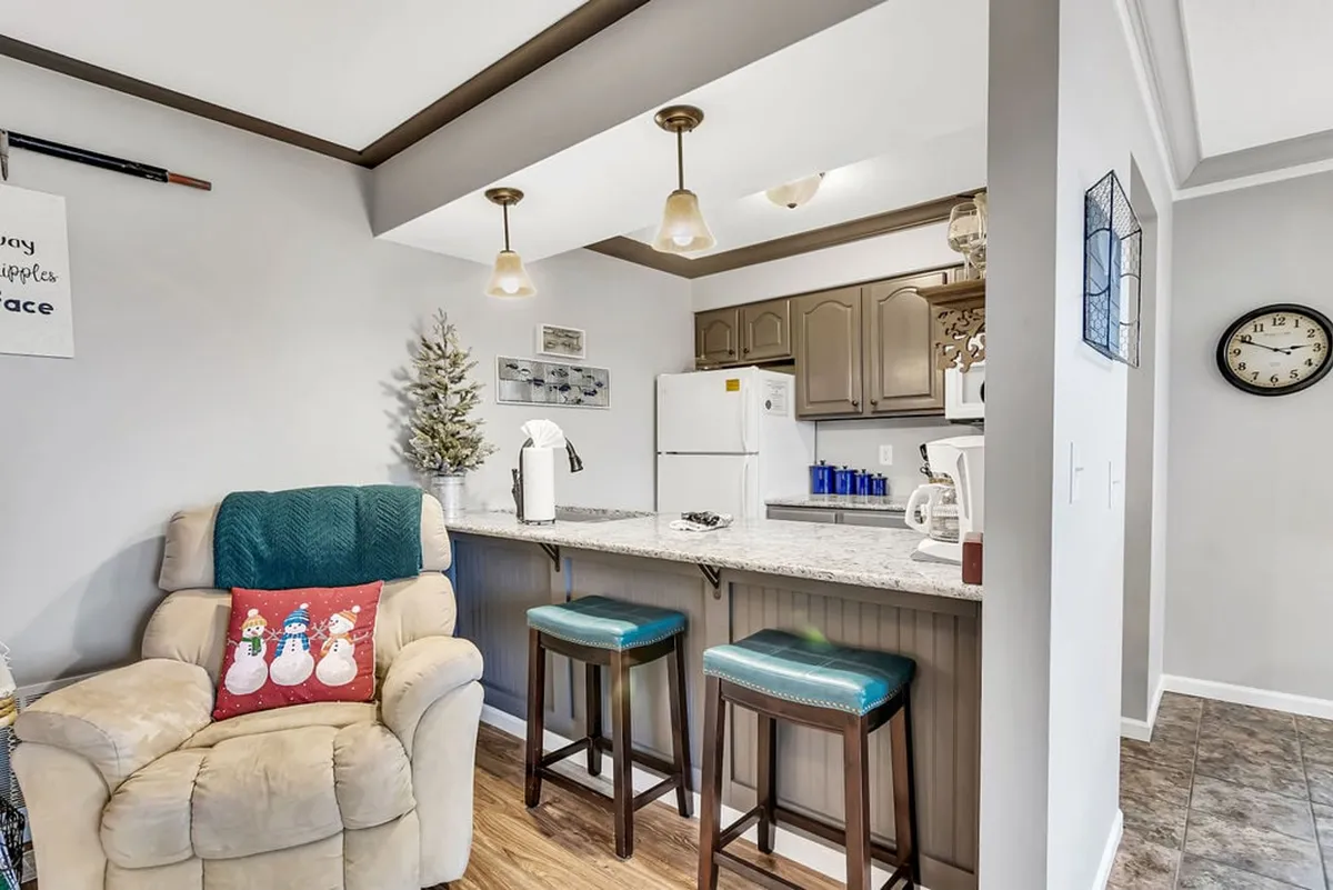 A cozy kitchen corner featuring bar stool seating at the kitchen island, sleek modern appliances, a decorative chair, and a festive small Christmas tree. The layout encourages casual dining, social interaction, and highlights the kitchen’s multifunctional use.