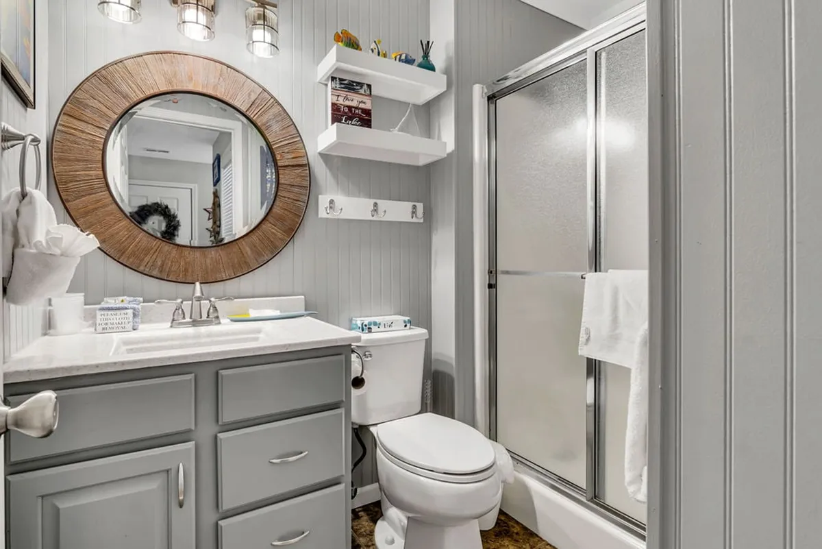 A modern bathroom with a large round mirror, contemporary light fixtures, and sleek gray cabinetry. The space feels fresh and bright, perfect for morning routines or unwinding after a day of adventure.