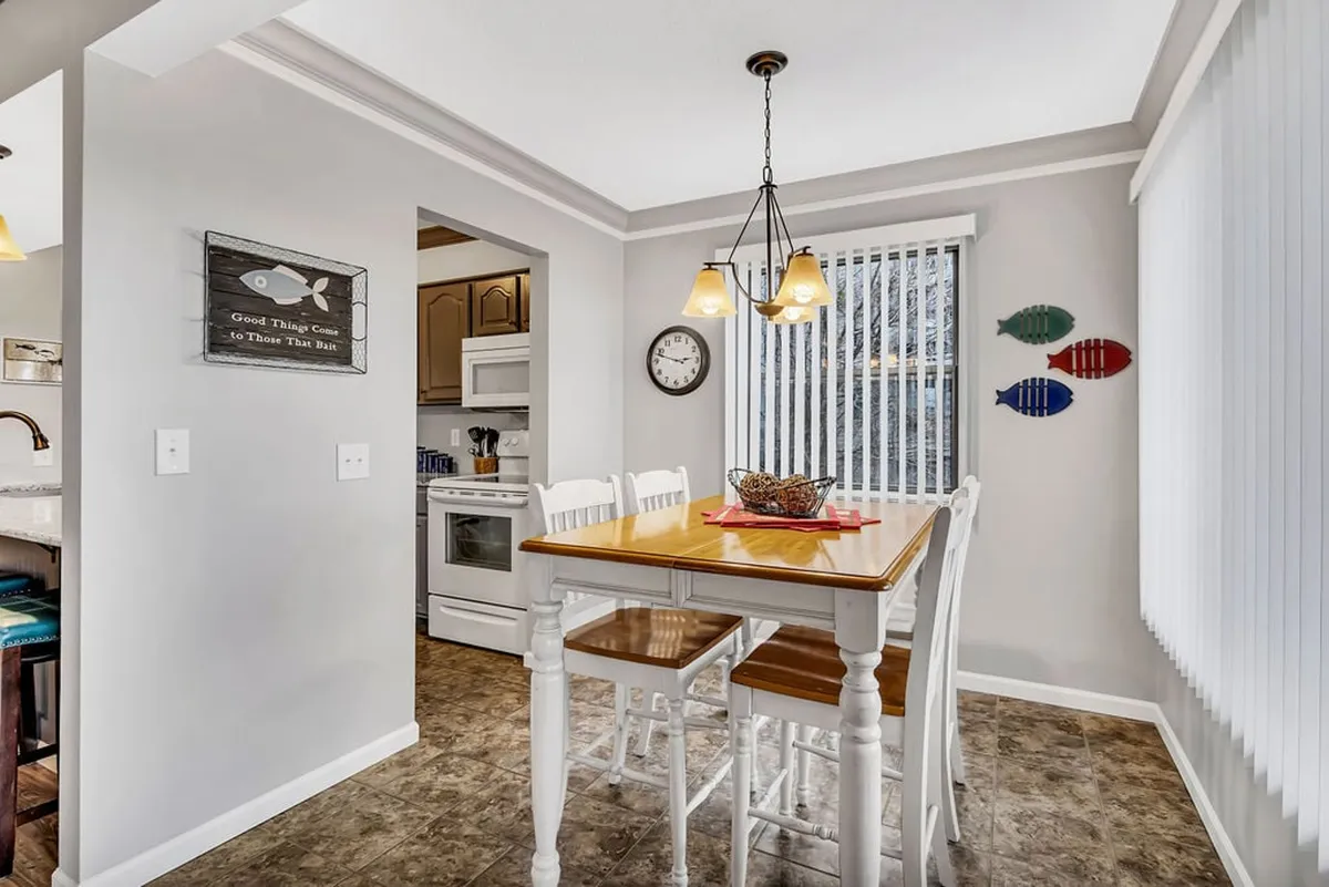 A cheerful dining area just off the kitchen, with a spacious wooden dining table, colorful fish-themed decorations, pendant lights, and a well-placed wall clock. The mood is bright and inviting, encouraging group meals and shared moments.