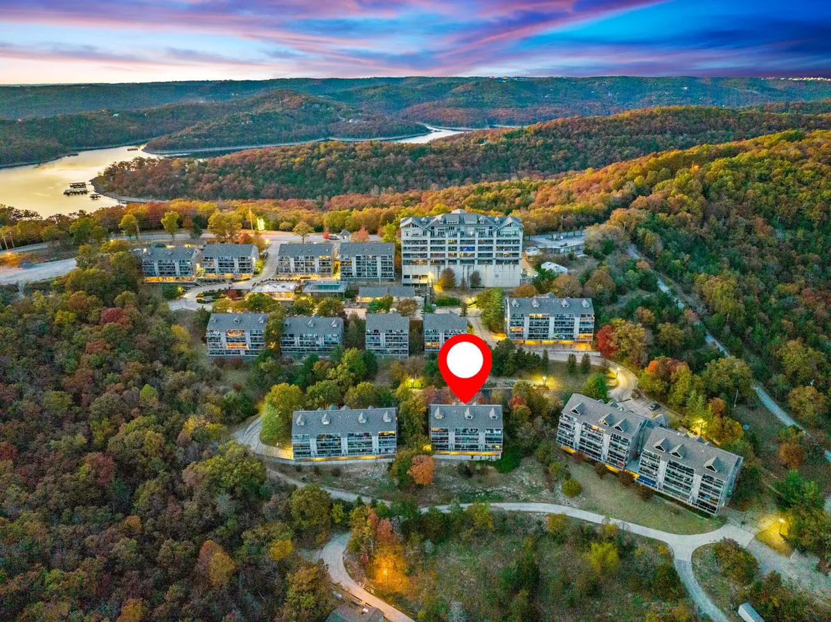 This image displays the scenic view of a lake surrounded by rolling hills, with condominium buildings and inviting walking paths in the foreground. The fall foliage adds warmth and vibrancy, and the tranquil water hints at leisure activities like boating and lakeside gatherings.